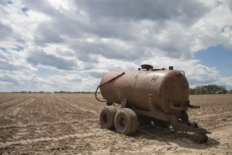 Sürülmüş tarlada duran paslı eski su tankı römorku